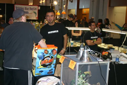 A busy vendor floor under heat lamps, tables of enclosures on both sides