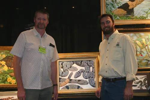Two artists in front of framed reptile paintings at their booth
